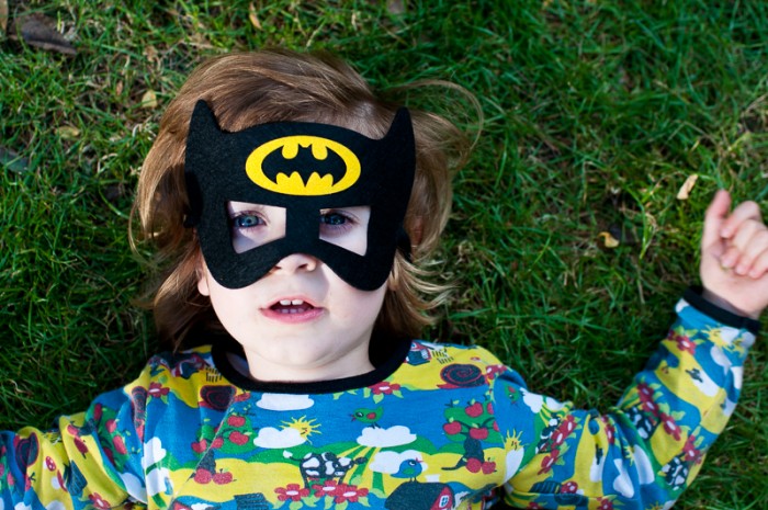 Little boy lying in the grass wearing batman mask