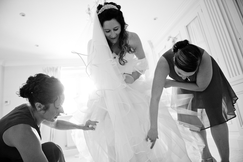 Black and white wedding photograph of bridesmaids helping bride into the dress