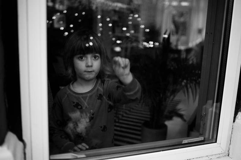 Boy looking out of the window in Bounds Green with Christmas lights reflected in the window