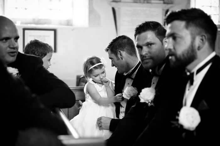 Black and white photo of little girl at church wedding sitting with ushers and best men