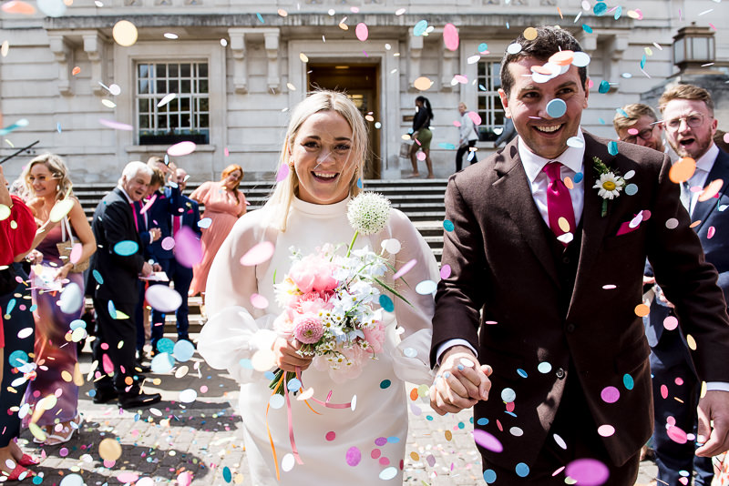 Bride and groom covered in colourful confetti outside Hackney Town Hall in East London.